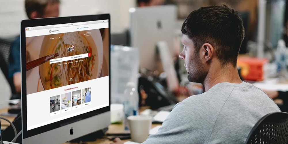 Man browsing Yelp for his business listing in open office environment.