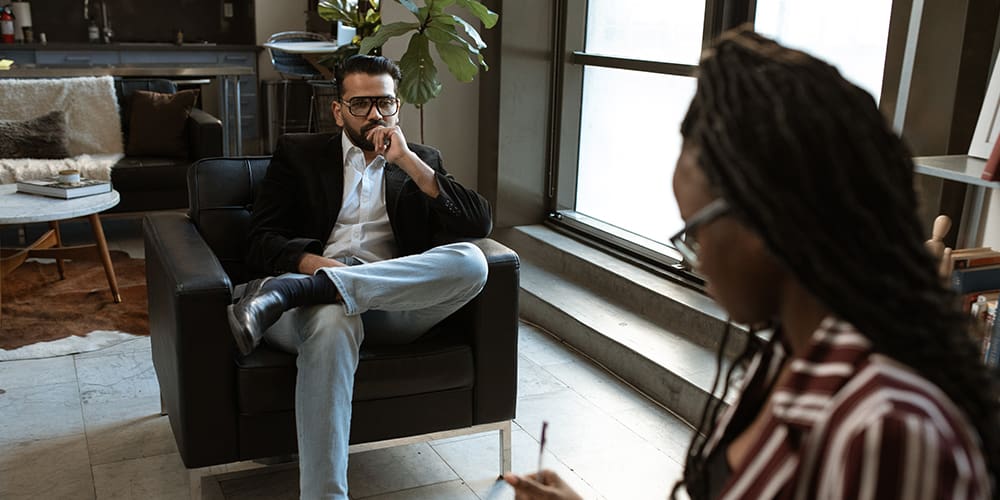 Employer look at a hiring candidate, seated across from each other while one takes notes to determine hiring employees.