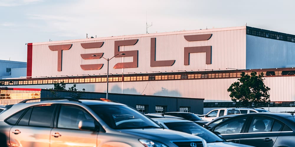 Tesla factory at sunset, with cars parked outside the building.