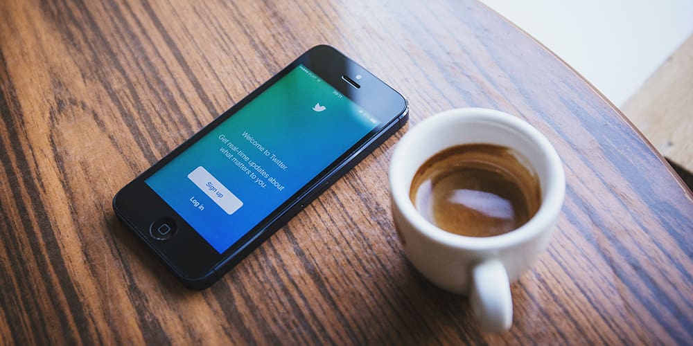 Twitter open on a smartphone on table next to a cup of warm brown tea.