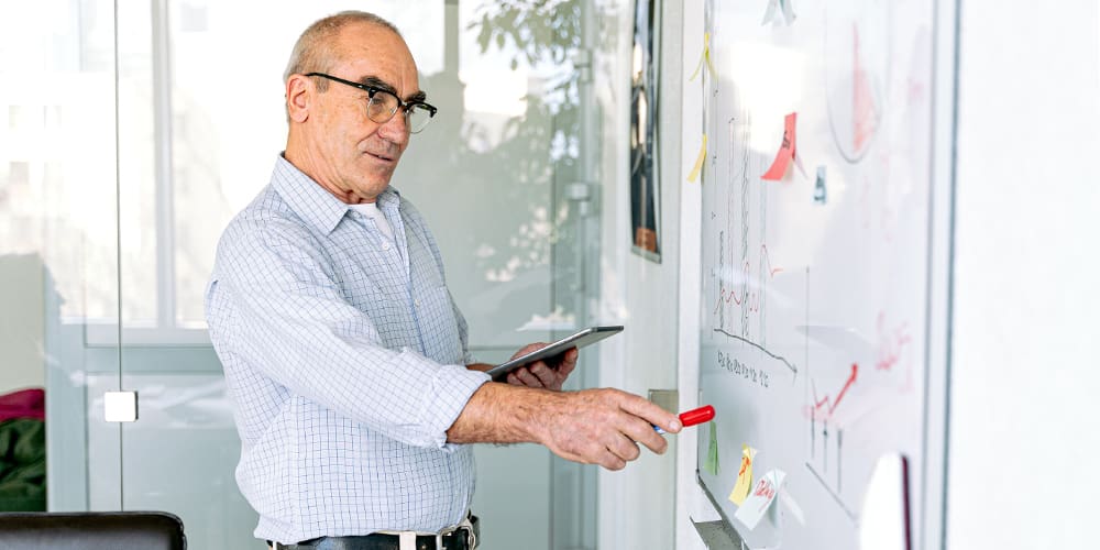 Older man in glasses using whiteboard at work representing age discrimination.
