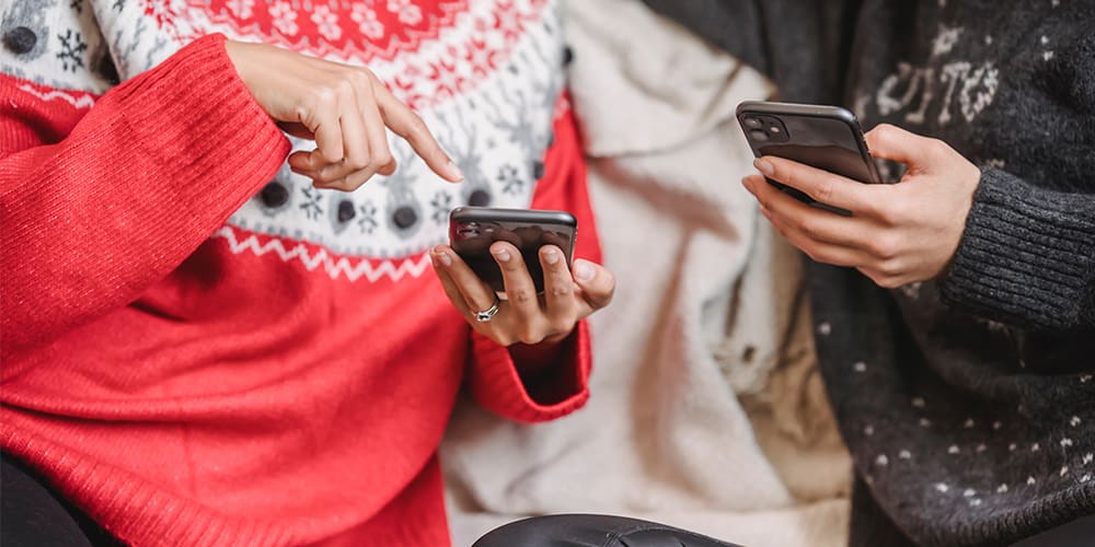 Two people sitting on a couch, pointing to phones to share millions on social media.