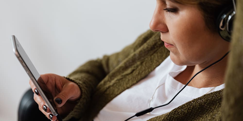 Woman in green cardigan and headphones listening to audio chat room on mobile, where Slack becomes a competitor.