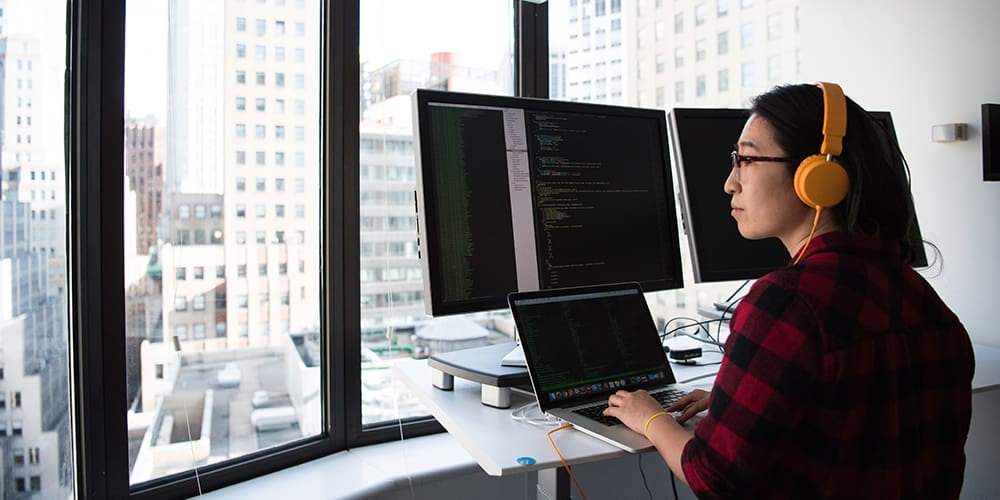 Quantum developer looking out of the window with a three monitor setup open to various coding programs.