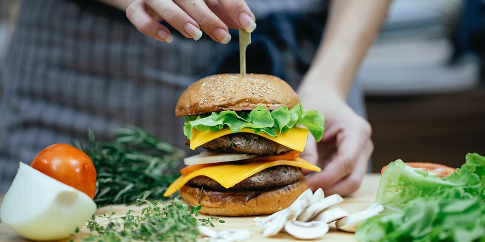 A professional chef making a home-cooked meal with a tall cheeseburger.