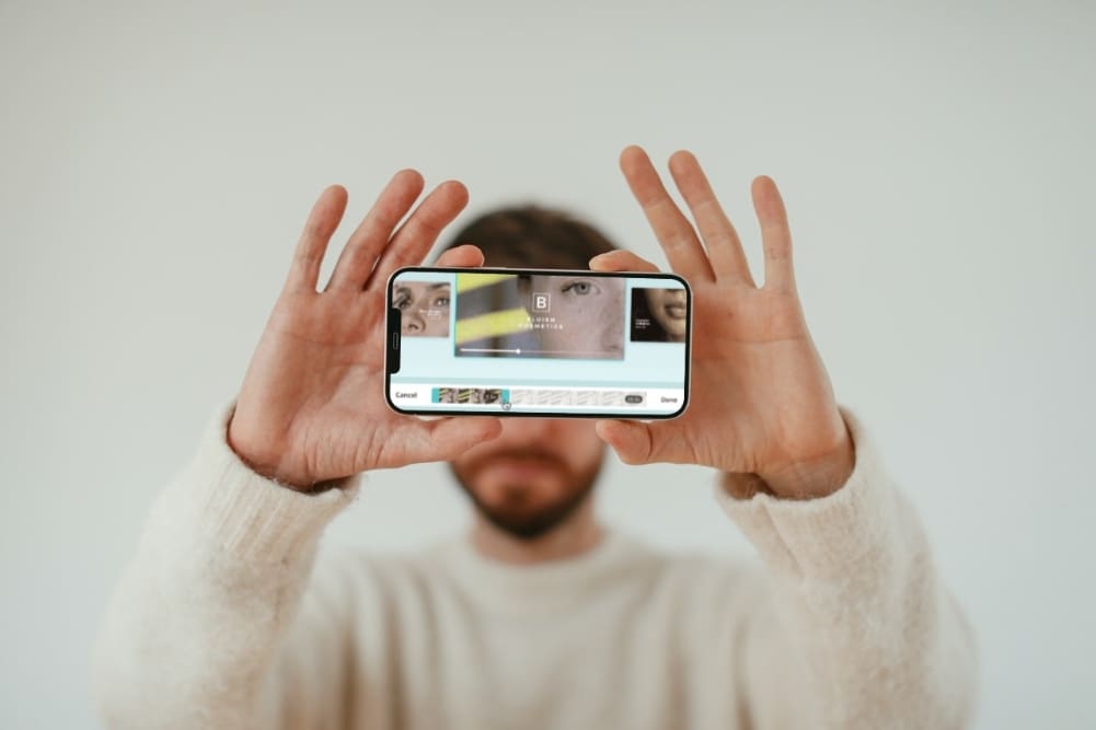 Caucasian man holding iPhone showing Canva video editor on mobile. 