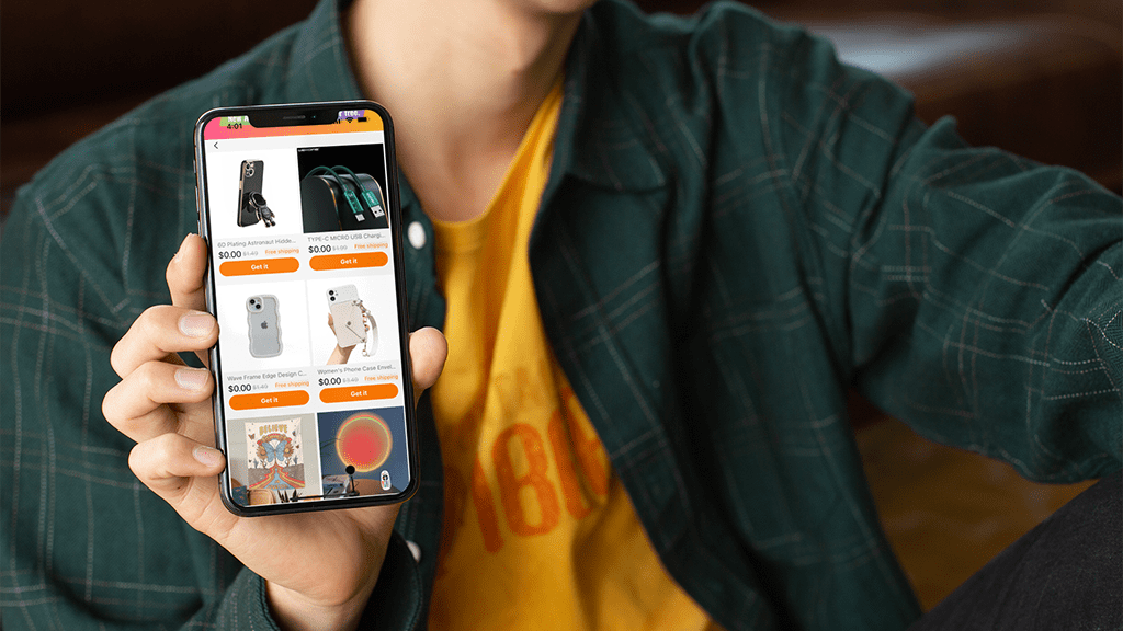 Temu A person in a green jacket and yellow holding up a smart phone to the viewer that is open to Temu app.