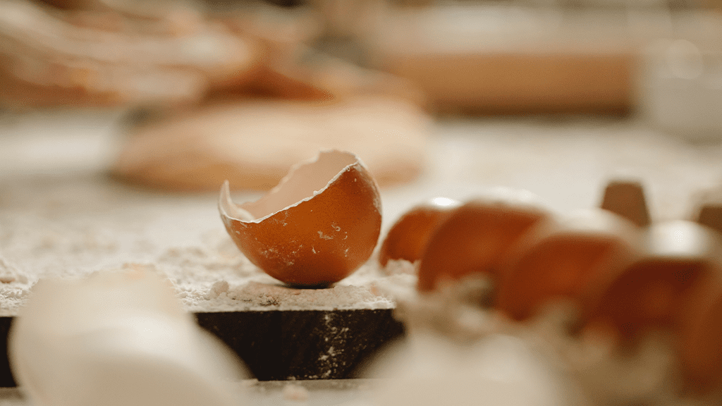 BrokenEggShell A carton of brown eggs from Dollar Tree sits next to a cutting board, with a broken open egg shell on the cutting board.