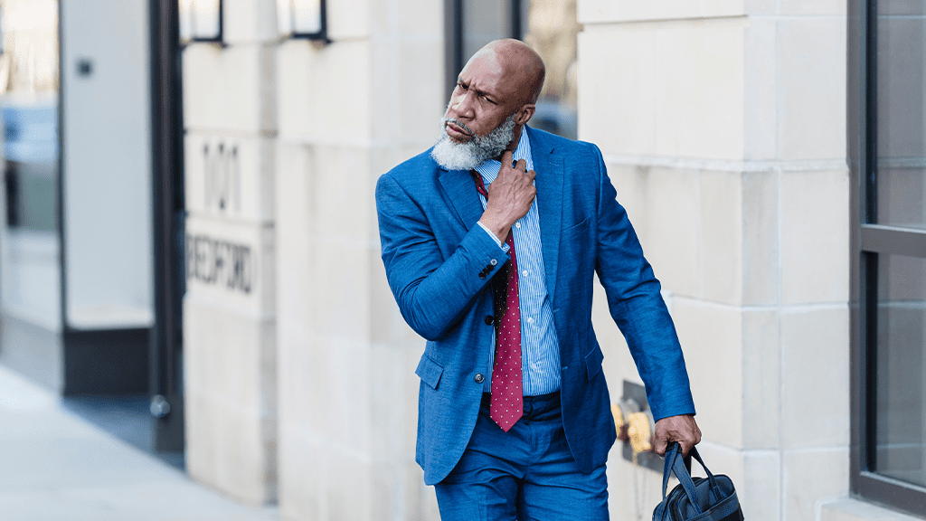 A Black man in a blue business suit carrying a briefcase adjusts his tie with a concerned looking following a Great Resignation moment.