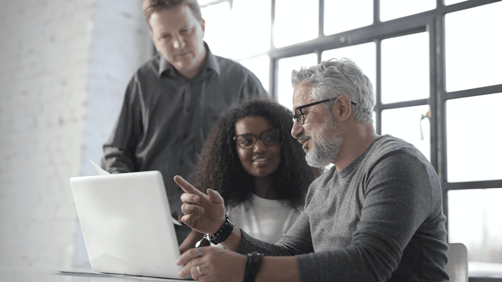 Several workers sit together, including a senior employee, as they talk about age discrimination in front of a computer, pointing at the screen for reference.