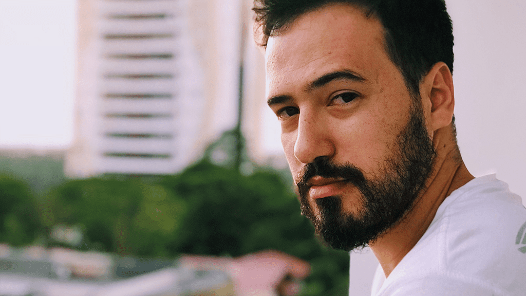 A man with a beard standing in front of a city skyline, looking at the camera. There religious accommodations to be considered.