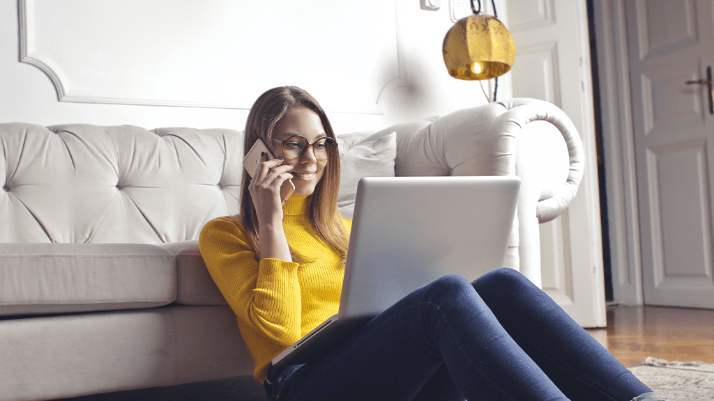 A woman in a yellow shirt sitting on the ground in front of a white couch on their laptop interacting with chat bots.