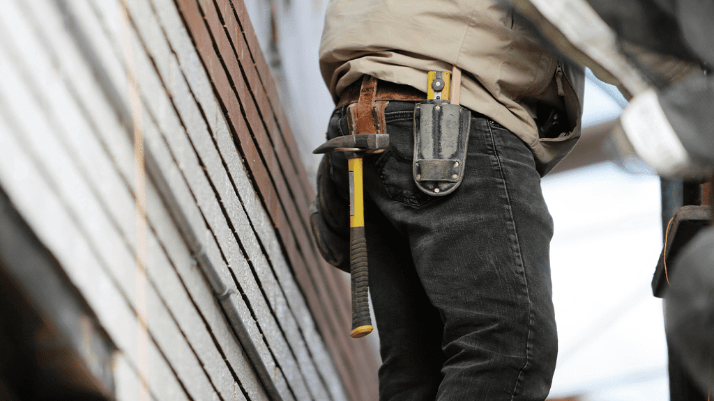 Focusing on construction contractor belt, with a half built wall behind them.