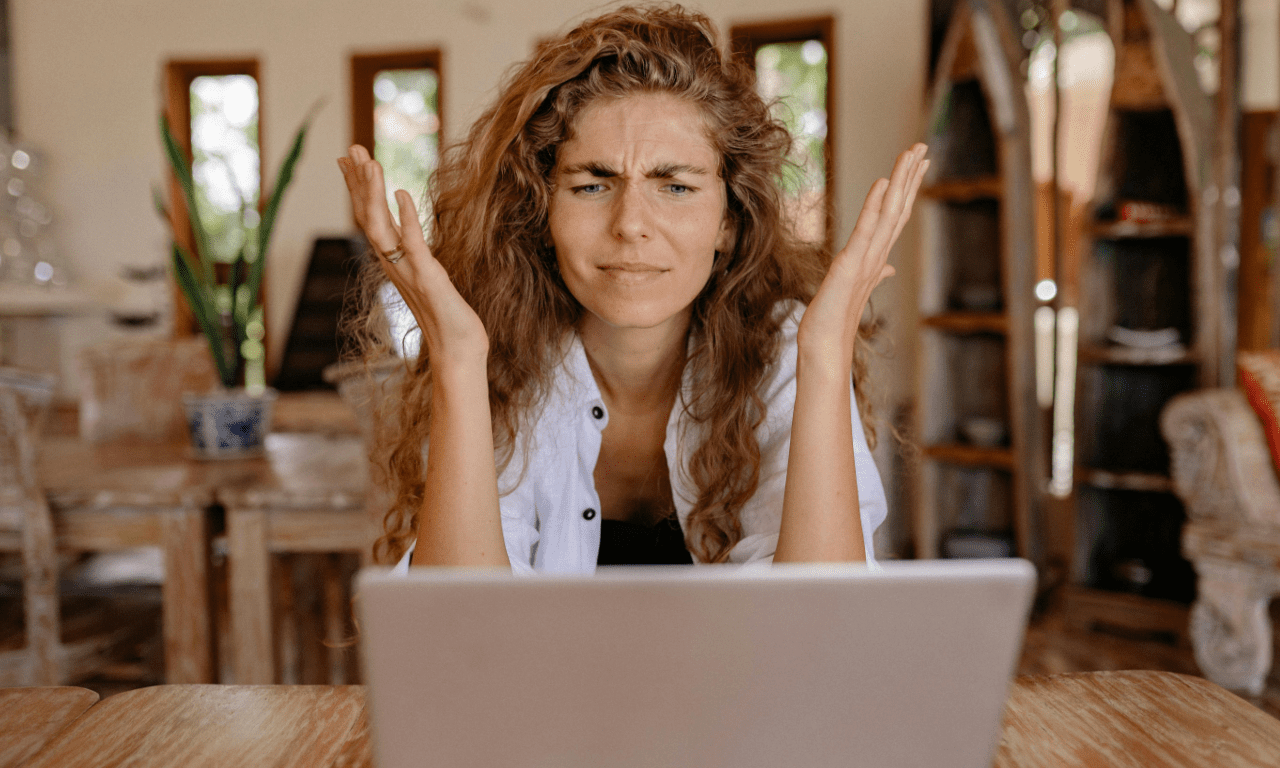 A woman with long curly hair looks at a laptop in front of her with an exasperated expression going through search results.