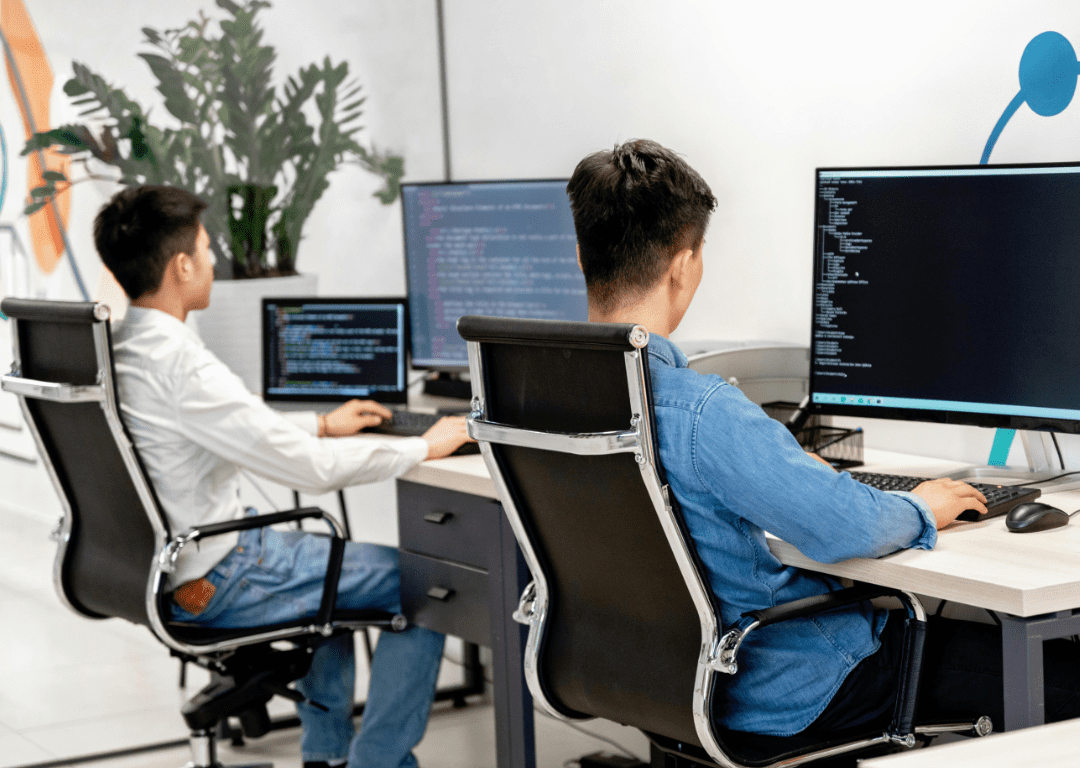 Return to office workers sitting at computers working on coding on computers in an open office layout.