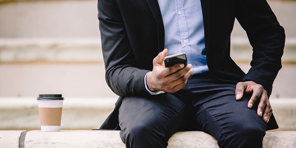 Person reading Twitter on phone seated on bench with coffee cup.