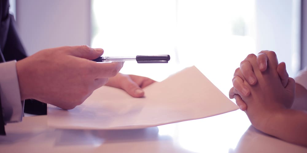 Mortgage papers held in hands with a pen, being handed to the other hands.