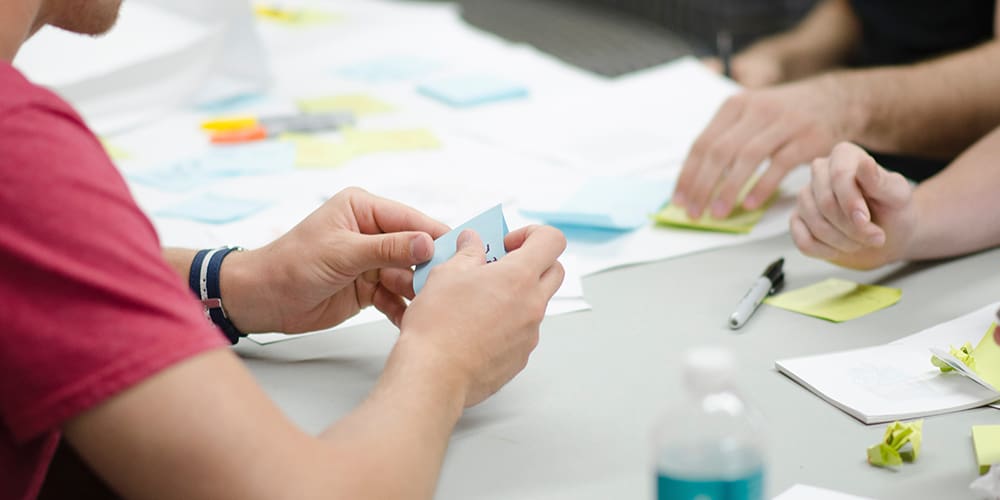 Two pairs of hands at a real estate startup meeting table with post-it notes.