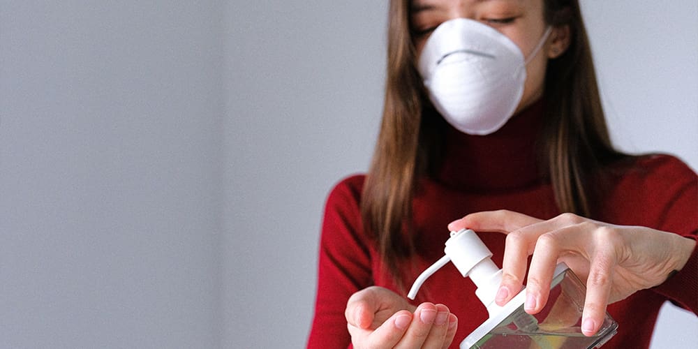 Woman with mask using hand sanitizer, part of COVID protocols