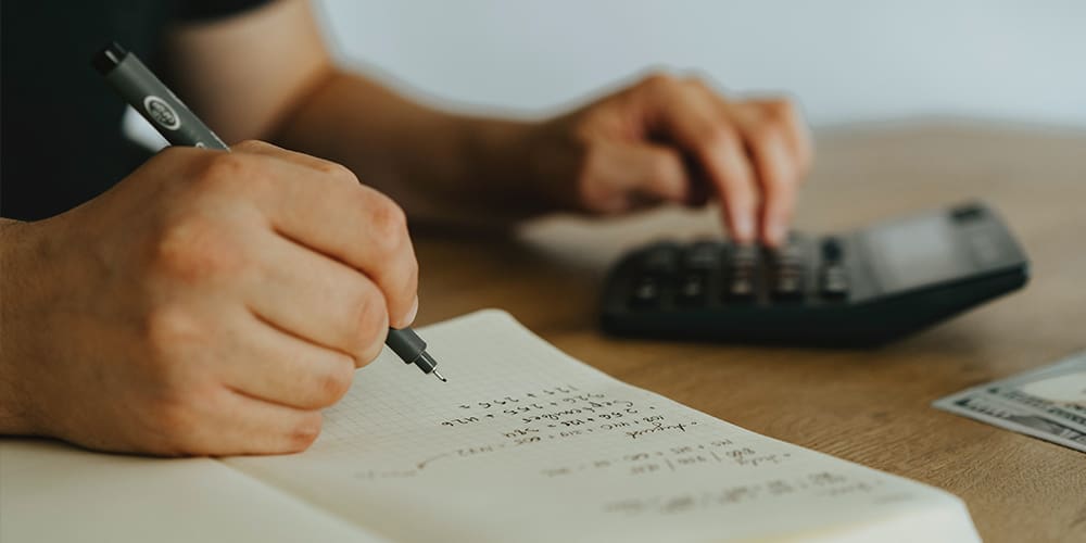 Hands on calculator and notebook while calculating standard deduction in taxes.