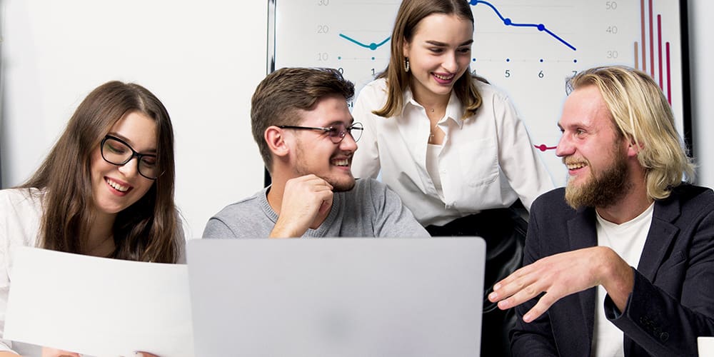 Four people around a computer with chart behind them talking with data visualization to guide them.