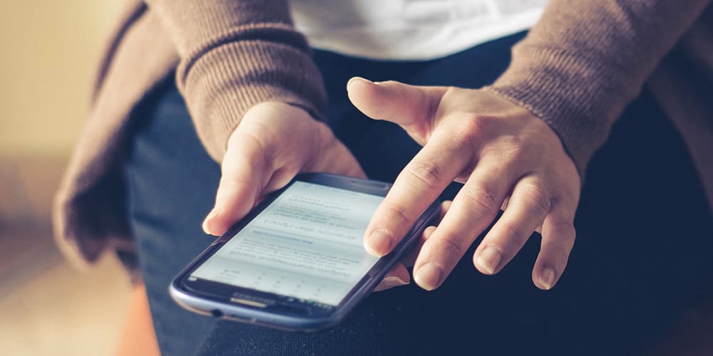 Woman holding phone in lap, doing an online home search.