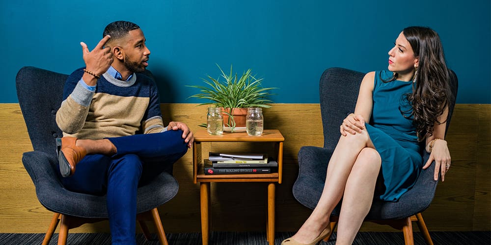 A Black man on the left and a white woman on the right deep in conversation in a blue and yellow room using the spin methods to have a conversation.