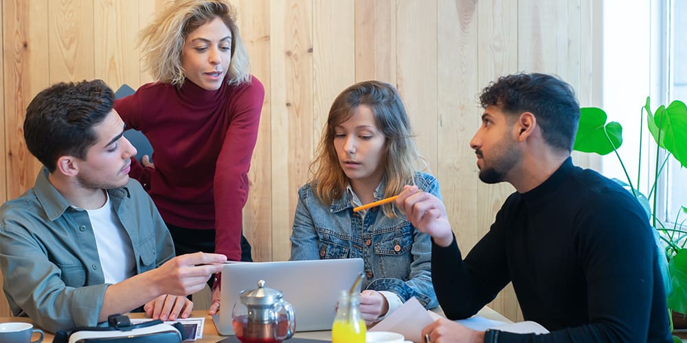 Freelancers and entrepreneurs working together in a meeting room, two men and two women, discussing over a laptop instead of starting an argument.