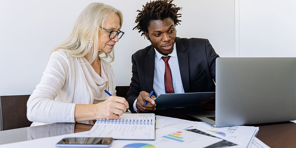 Realtors across demographics looking at data on laptop with papers scattered across desk.