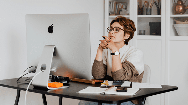 A woman sits in front of a desktop computer with a critical expression as she reads through an email to detect scams