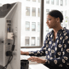 A Black woman sits and working at a computer, checking Reddit.