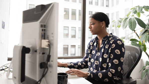 A Black woman sits and working at a computer, checking Reddit.