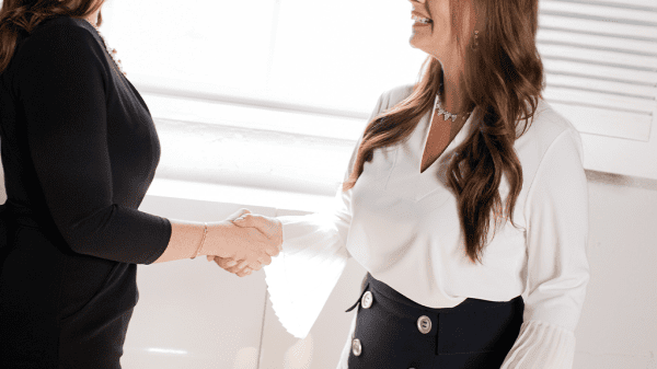 Two women shake hands in a friendly business manner. One woman is smiling boradly at the agreed deal, but remember vanity metrics can exist anywhere.