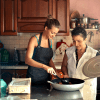 A mother and daughter cook together in a warmly decorated kitchen, part of a trend of multi-generational housing.