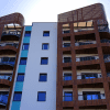 A ground view looking up at a modern set of apartment housing with the sun glowing behind it.