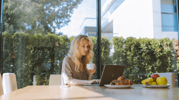 A woman sits at a laptop in a warmly lit kitchen with free time at a home work.