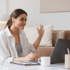 A woman waves at the laptop with airpods in as she checks in for daily stand-ups.