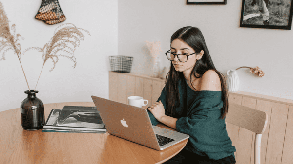 A woman sits at a desk with a laptop and a brushy plant sits next to her as she browses paid search conversions.