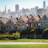 A view of houses in a suburb clustered together, with a city skyline in the distance behind the line of houses.