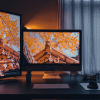 A set of two desktop monitors displays a brick house and orange leaves behind it, showing digital real estate on their computer sitting on top of a modern dark desk.