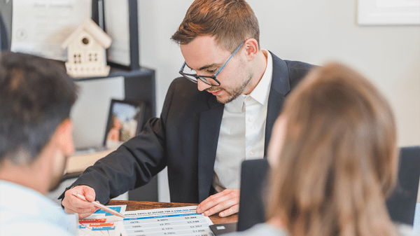 A real estate agent reviews paperwork for some clients who are seated in the foreground.