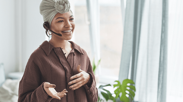 A real estate agent, a woman with her hair wrapped up in a neat cloth on her head, talks on the phone with a hands free setup.
