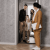 A family enters one of the cheapest houses in their local area, with gray modern patterned wallpaper and a real estate agent beckoning them inside.