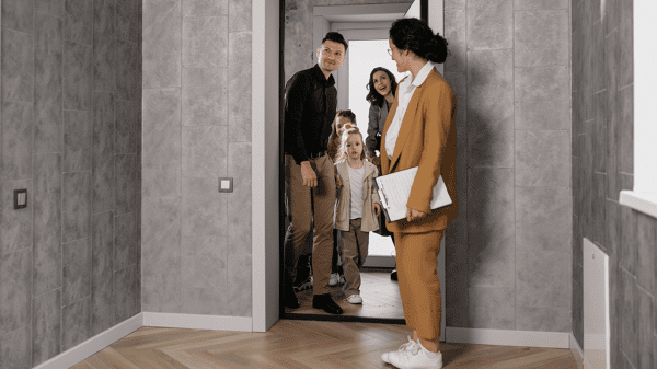 A family enters one of the cheapest houses in their local area, with gray modern patterned wallpaper and a real estate agent beckoning them inside.