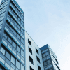 A skyward pointing view of two tall office buildings against a cloudy blue sky.