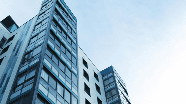 A skyward pointing view of two tall office buildings against a cloudy blue sky.